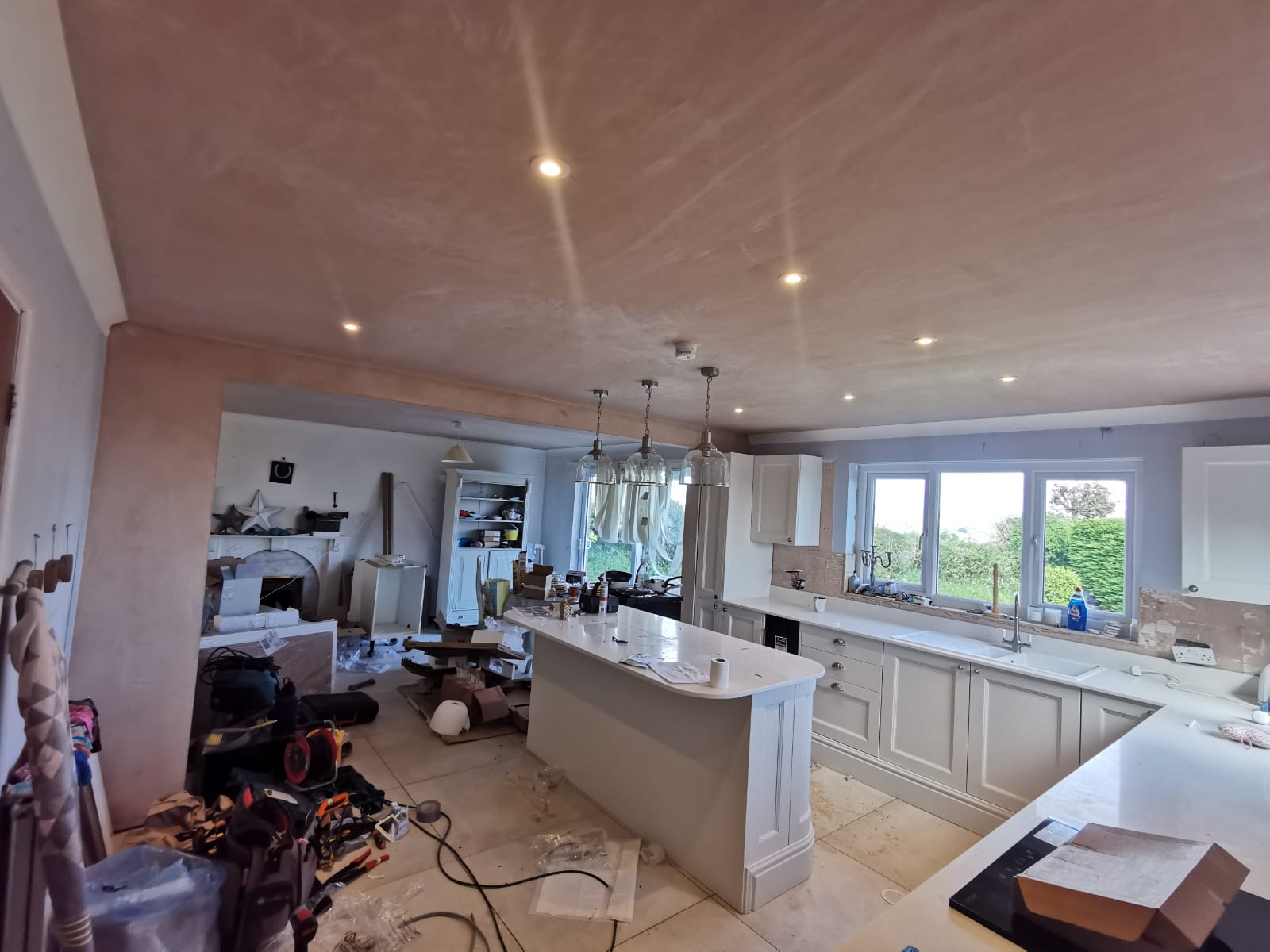 Open-plan kitchen part way through, with new downlights and three glass pendants over the island