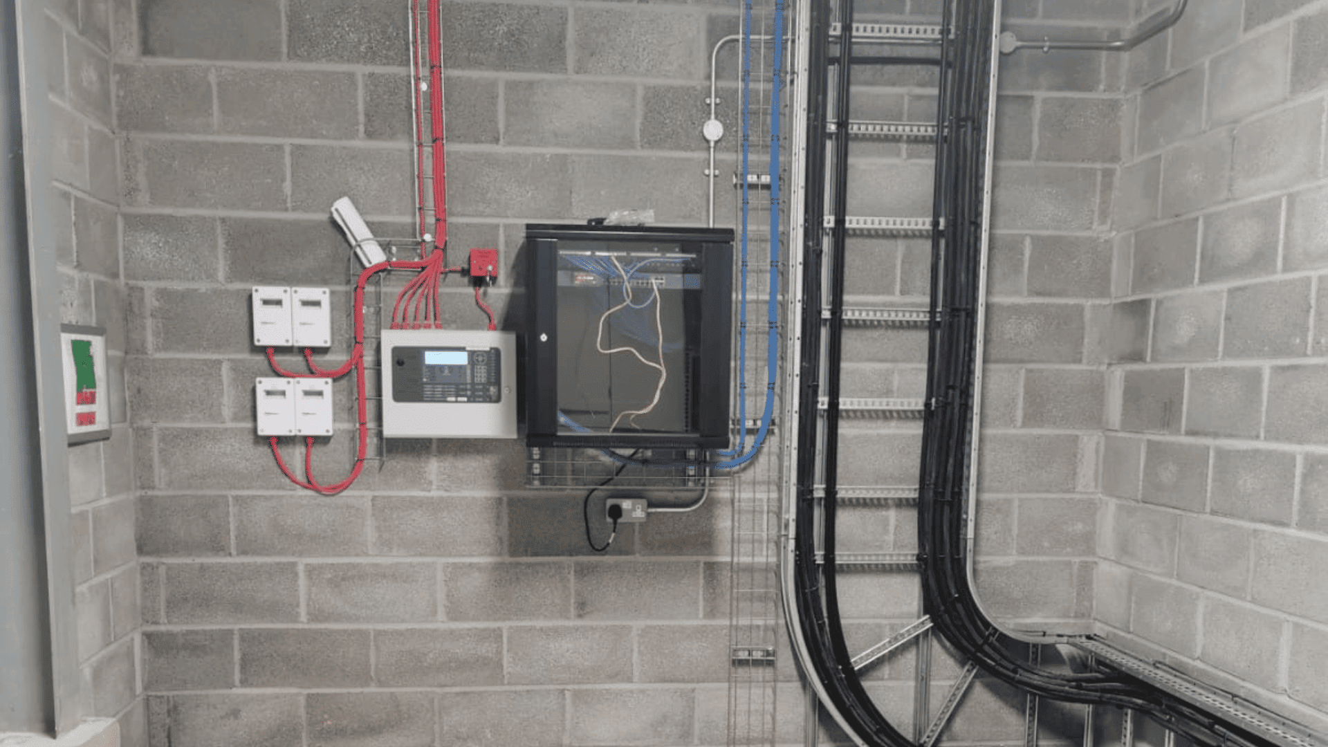 Plant room with a control panel, red fire-rated cabling and cables on tray against blockwork