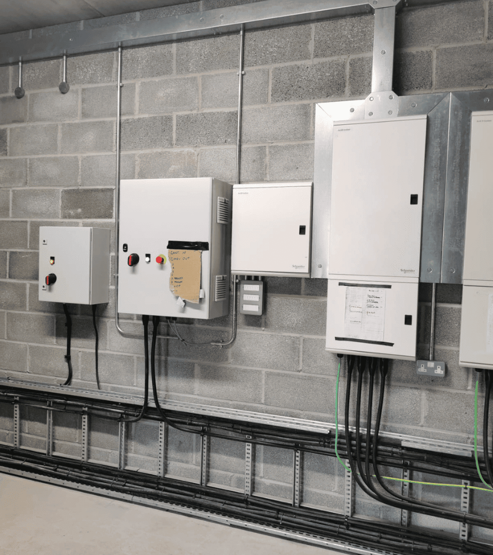 Industrial distribution boards and isolators on a blockwork wall, with cables on ladder tray below