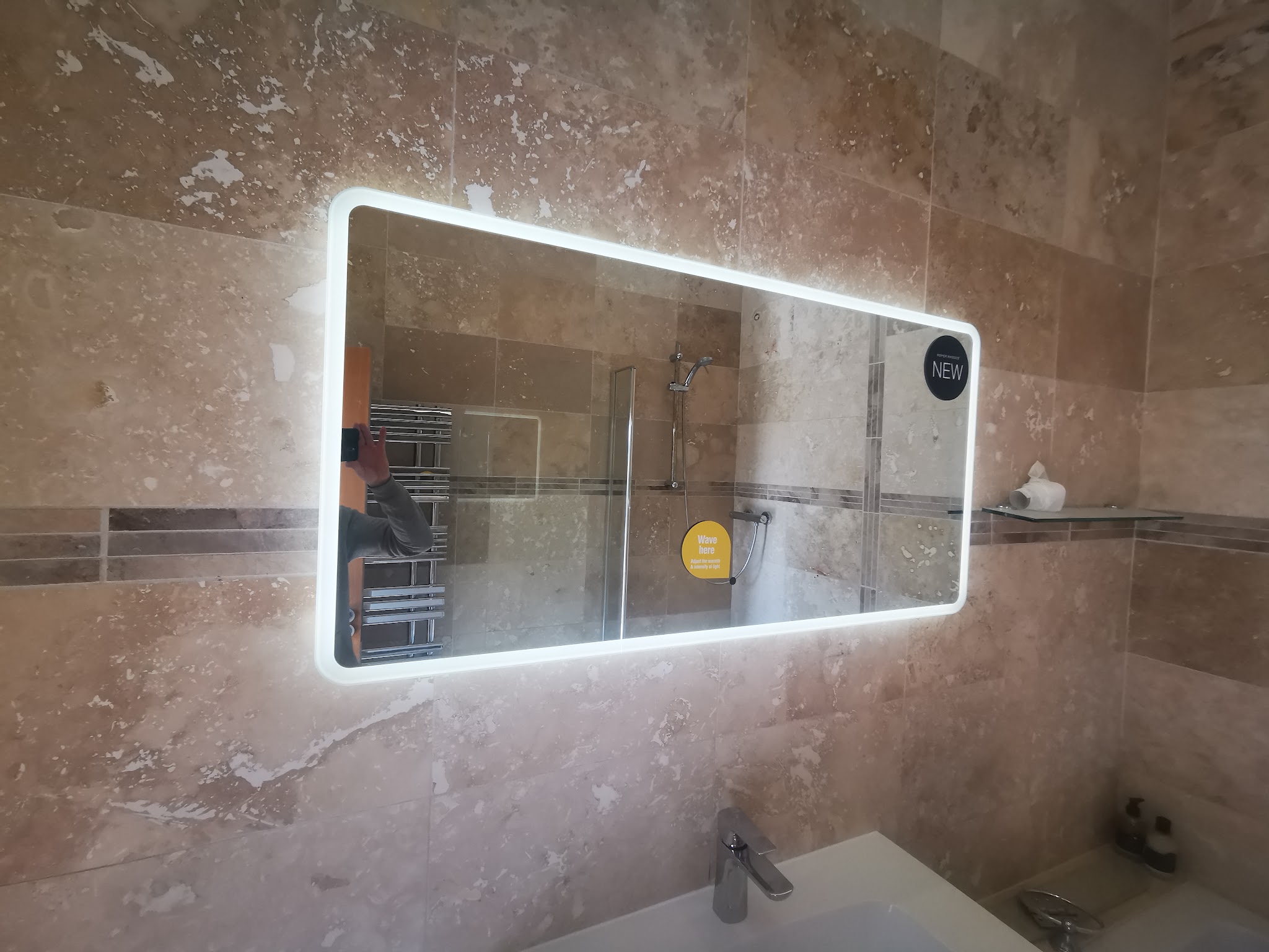 Illuminated LED mirror fitted on a travertine-tiled bathroom wall